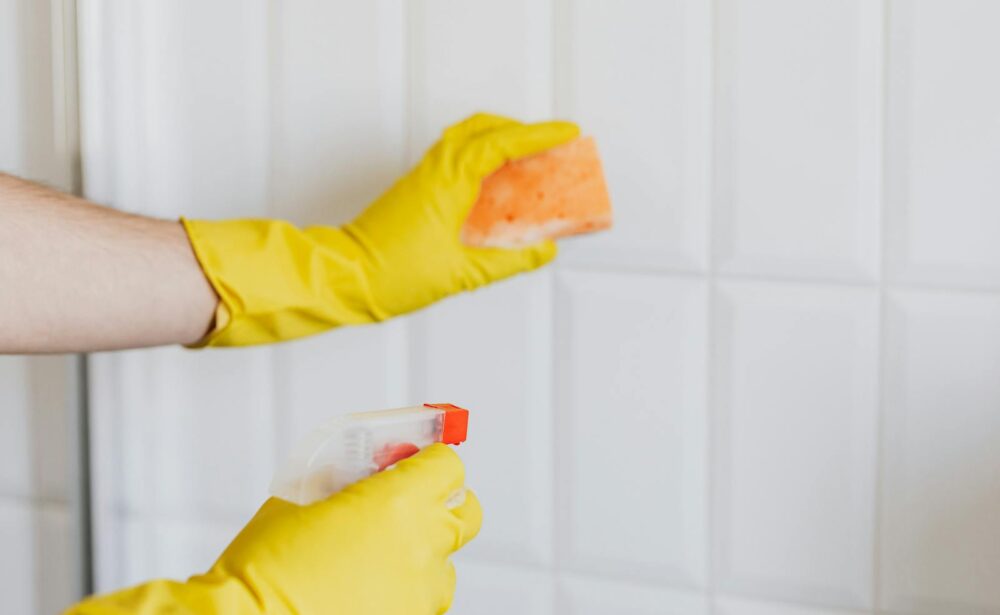 Hands in yellow gloves cleaning tiles with spray bottle and sponge