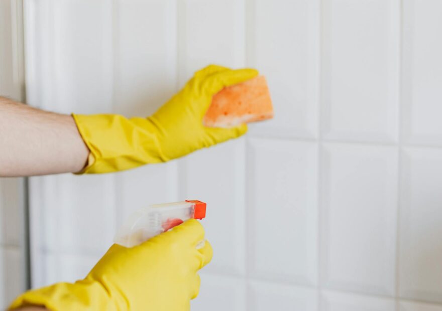 Hands in yellow gloves cleaning tiles with spray bottle and sponge